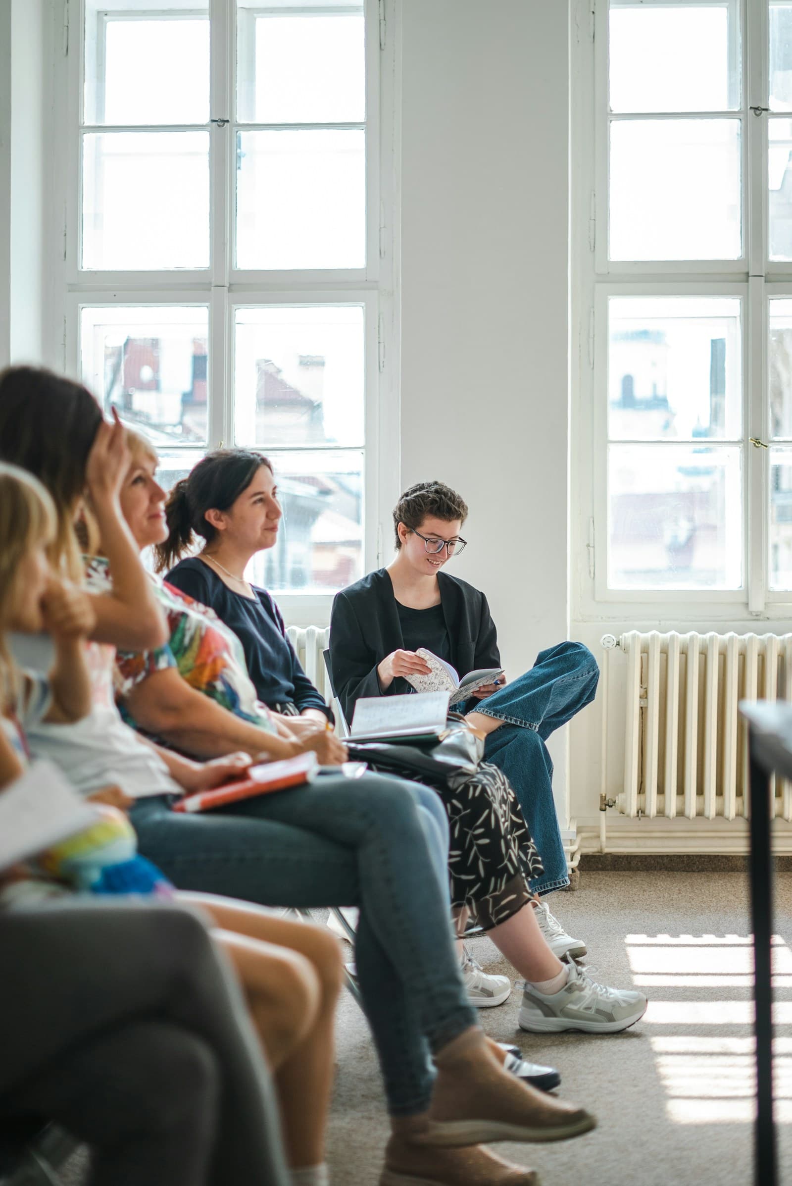 Adultos sentados numa sala luminosa, a ouvir e a tomar notas durante uma aula